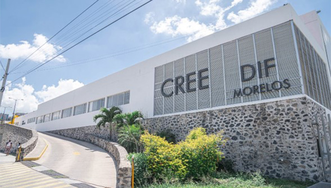 La imagen muestra una prolongada pendiente de concreto con vegetación a su costado derecho. Esta rampa sirve como ingreso a una edificación de color blanco con una leyenda que dice: CREE DIF MORELOS.