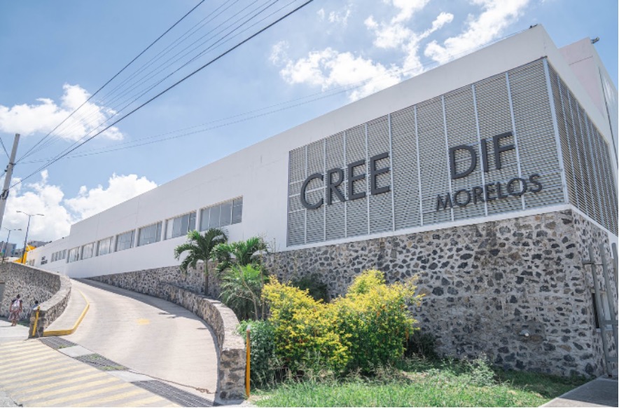 La imagen muestra una prolongada pendiente de concreto con vegetación a su costado derecho. Esta rampa sirve como ingreso a una edificación de color blanco con una leyenda que dice: CREE DIF MORELOS.